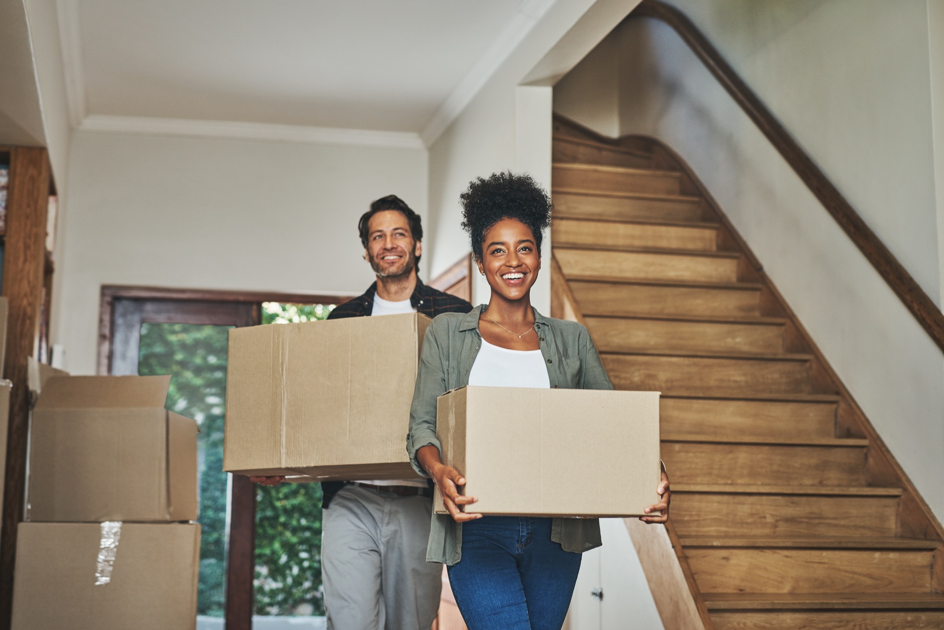 Couple heureux, immobilier et emménagement dans une nouvelle maison avec cartons pour rénovation, investissement ou déménagement. Un couple mixte transporte des cartons pour louer un bien, obtenir un prêt immobilier ou déménager ensemble.